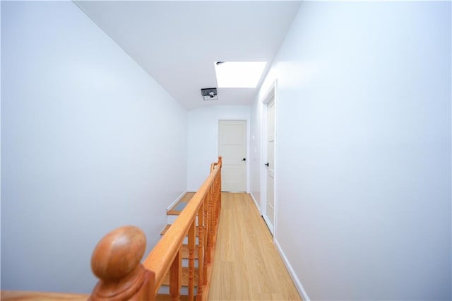 corridor featuring light wood-type flooring, an upstairs landing, and baseboards