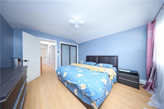 bedroom with vaulted ceiling, a baseboard heating unit, light wood-style floors, and a closet