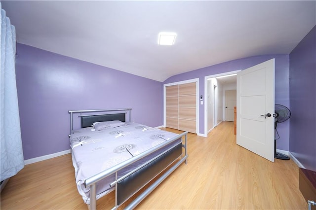 bedroom featuring lofted ceiling, light wood finished floors, a closet, and baseboards