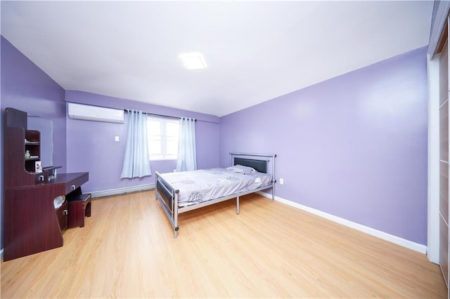 bedroom featuring an AC wall unit, light wood finished floors, and baseboards