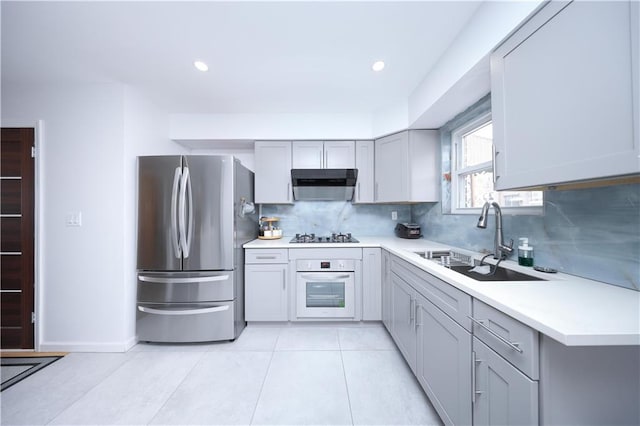 kitchen featuring oven, freestanding refrigerator, a sink, under cabinet range hood, and gray cabinetry