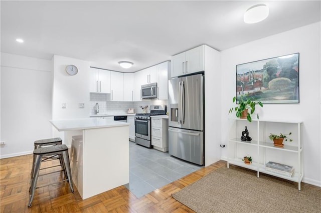 kitchen featuring a breakfast bar, light countertops, decorative backsplash, stainless steel appliances, and a sink