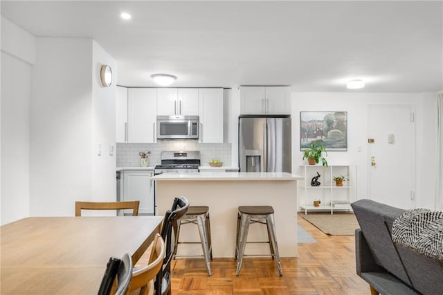 kitchen with light countertops, appliances with stainless steel finishes, a kitchen bar, white cabinetry, and backsplash