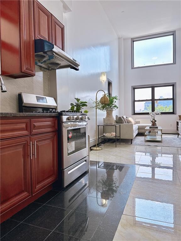 31-47 137th St Unit 4B, Brooklyn, NY 11354 - kitchen with stainless steel gas range, a high ceiling, dark brown cabinets, under cabinet range hood, and dark countertops