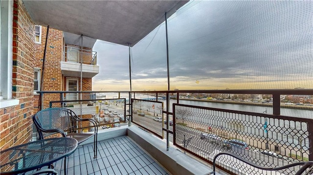 balcony at dusk featuring a water view