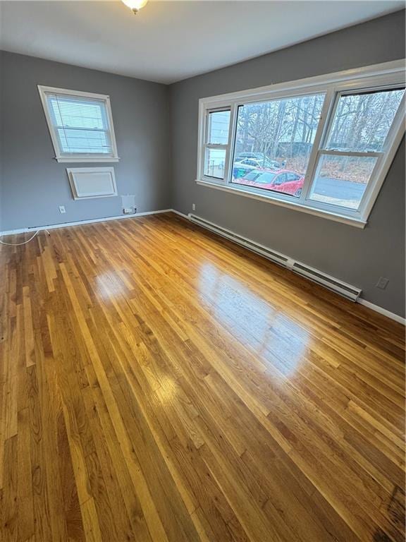 empty room featuring baseboards, a baseboard heating unit, and wood finished floors