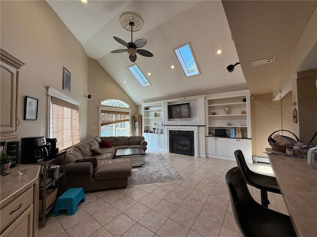 living room with light tile patterned floors, a ceiling fan, a fireplace, a skylight, and high vaulted ceiling
