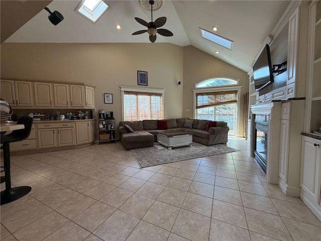 living room featuring high vaulted ceiling, light tile patterned floors, a ceiling fan, a glass covered fireplace, and a skylight
