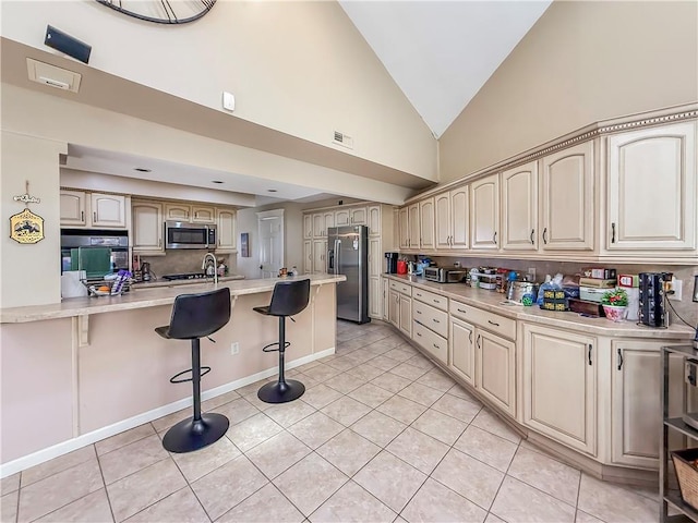 kitchen with a peninsula, light tile patterned floors, light countertops, a breakfast bar area, and appliances with stainless steel finishes