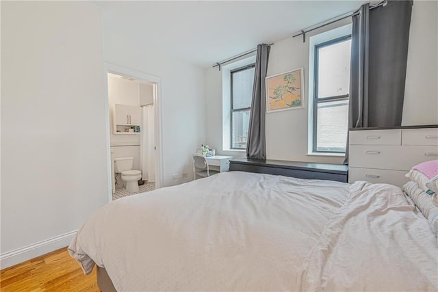 bedroom with multiple windows, light wood-type flooring, connected bathroom, and baseboards