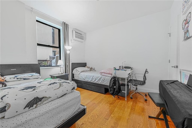 bedroom featuring a wall unit AC, wood finished floors, and baseboards