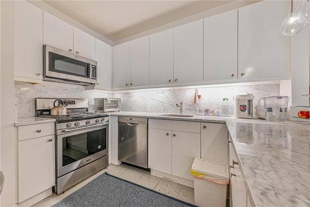 kitchen featuring appliances with stainless steel finishes, tasteful backsplash, light stone counters, and white cabinetry