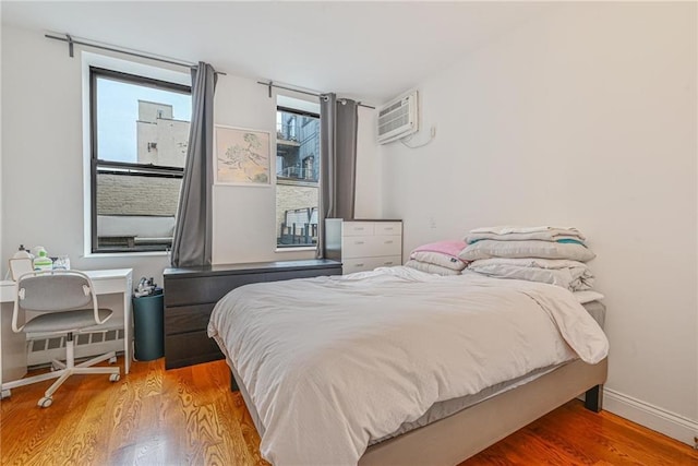 bedroom with wood finished floors, baseboards, and a wall mounted AC