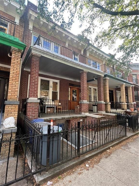 rear view of property featuring brick siding, a balcony, and fence