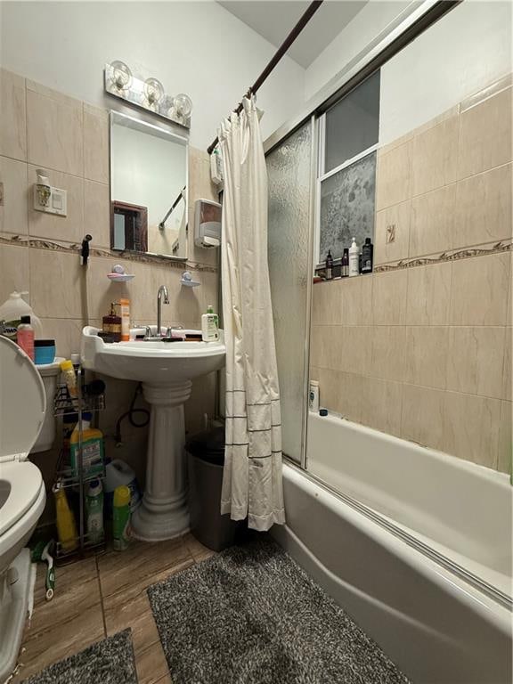 bathroom featuring toilet, wood finished floors, shower / bath combo with shower curtain, and tile walls