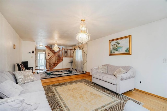 living area with wood finished floors, baseboards, a notable chandelier, and stairs