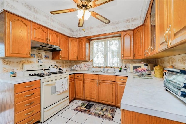 kitchen with a sink, brown cabinets, white appliances, light countertops, and under cabinet range hood