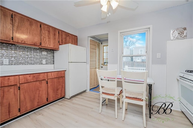 kitchen featuring decorative backsplash, wainscoting, white appliances, ceiling fan, and light wood finished floors