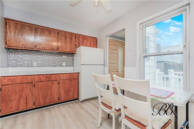 kitchen featuring brown cabinetry, freestanding refrigerator, light countertops, a ceiling fan, and backsplash