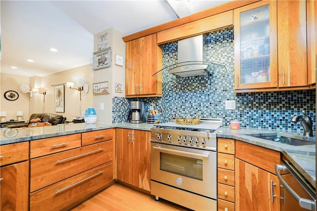 kitchen featuring light stone counters, a sink, appliances with stainless steel finishes, and wall chimney range hood