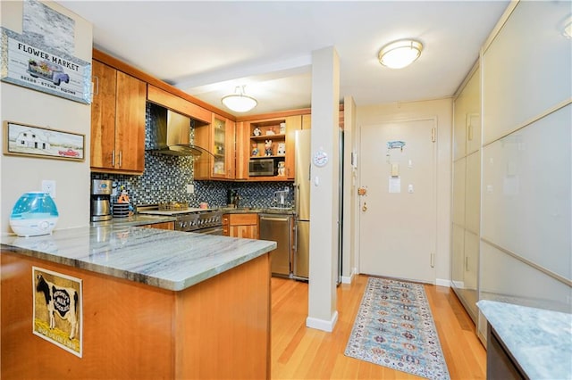 kitchen featuring wall chimney range hood, brown cabinets, appliances with stainless steel finishes, light wood-type flooring, and a peninsula