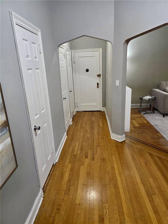 hall with hardwood / wood-style floors, baseboards, and arched walkways