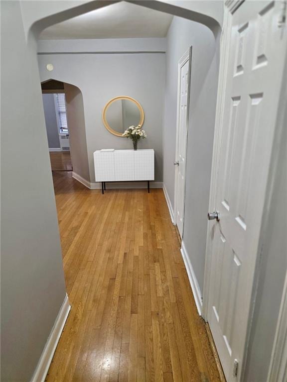 hall featuring baseboards, arched walkways, and hardwood / wood-style flooring