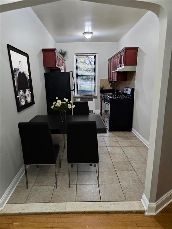 kitchen with under cabinet range hood, dark brown cabinets, baseboards, radiator heating unit, and appliances with stainless steel finishes