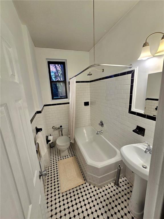 bathroom with toilet, a wainscoted wall, shower / tub combo, tile patterned floors, and tile walls