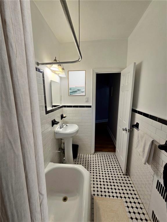 bathroom featuring a shower with curtain, tile walls, a bathtub, tile patterned flooring, and a wainscoted wall