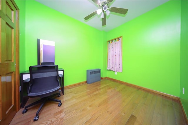 office space featuring baseboards, heating unit, ceiling fan, and light wood-style flooring