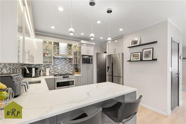 kitchen with tasteful backsplash, light wood-style flooring, a peninsula, wall chimney range hood, and appliances with stainless steel finishes