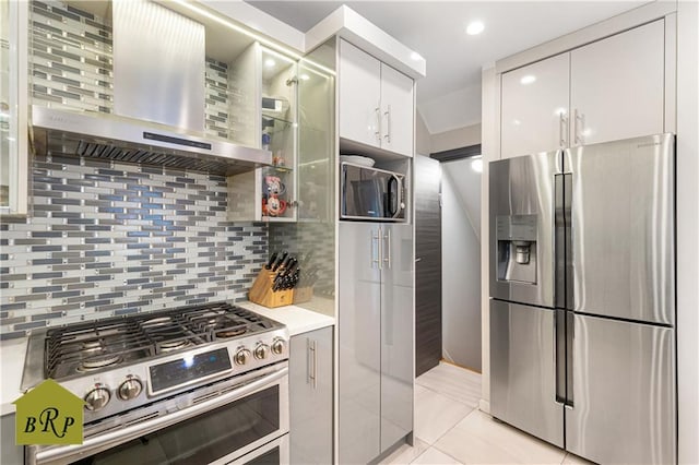 kitchen featuring stainless steel appliances, light countertops, wall chimney range hood, backsplash, and modern cabinets