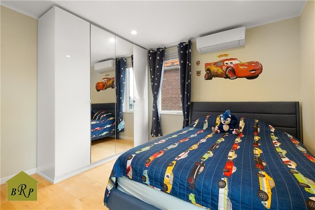 bedroom with wood finished floors, a wall unit AC, and baseboards