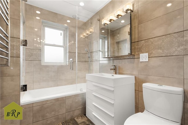 bathroom with tile walls, tiled shower / bath, toilet, and vanity