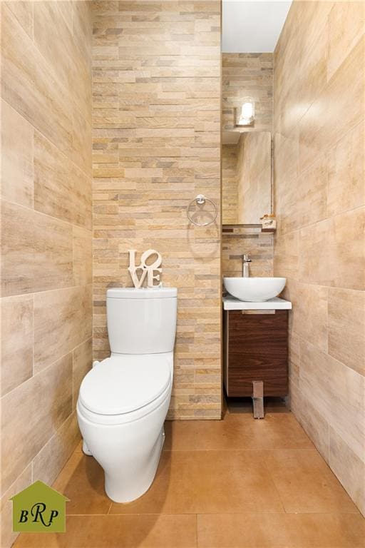 half bath featuring toilet, vanity, and tile walls