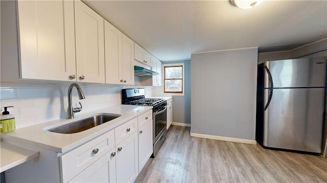 kitchen featuring light wood-style flooring, tasteful backsplash, appliances with stainless steel finishes, under cabinet range hood, and a sink