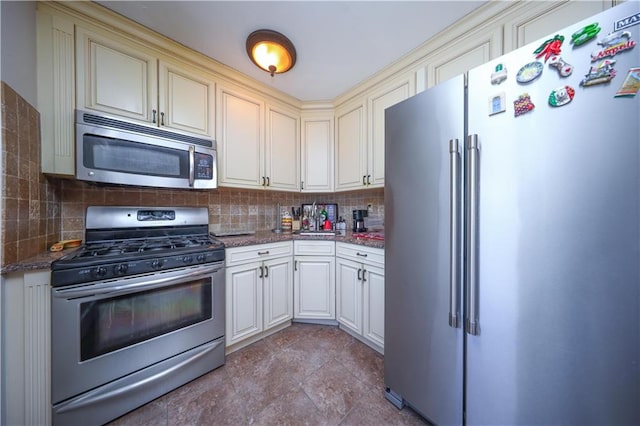 kitchen featuring dark stone countertops, backsplash, cream cabinetry, and stainless steel appliances