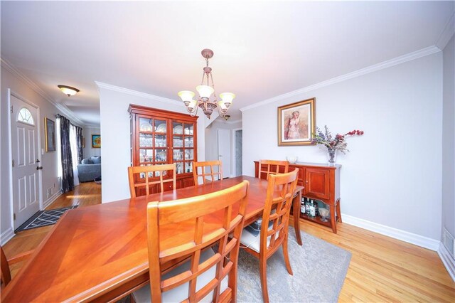 dining space with crown molding, baseboards, a notable chandelier, and light wood finished floors
