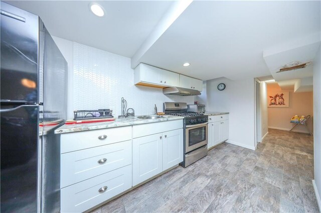 kitchen featuring freestanding refrigerator, white cabinets, under cabinet range hood, and stainless steel range with gas stovetop