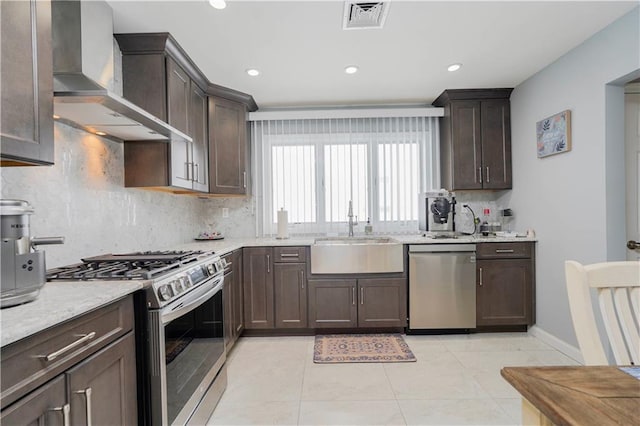 kitchen featuring dark brown cabinets, visible vents, wall chimney exhaust hood, appliances with stainless steel finishes, and a sink