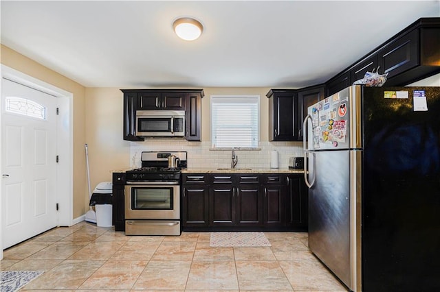 kitchen with light stone countertops, tasteful backsplash, a sink, stainless steel appliances, and dark cabinetry