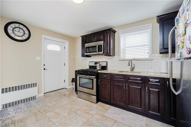 kitchen featuring radiator, dark brown cabinetry, appliances with stainless steel finishes, a sink, and decorative backsplash