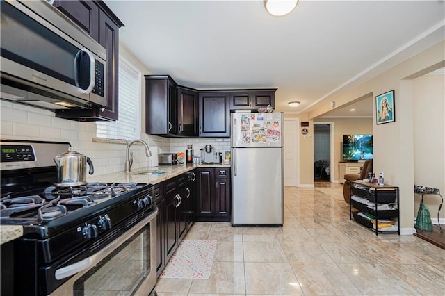 kitchen with baseboards, light stone countertops, decorative backsplash, stainless steel appliances, and a sink