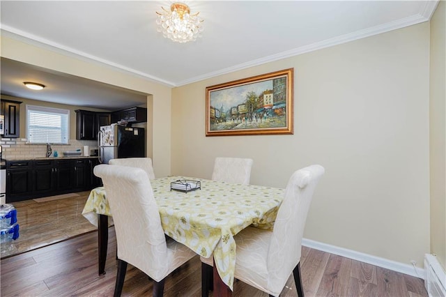 dining area with baseboard heating, crown molding, a notable chandelier, and wood finished floors