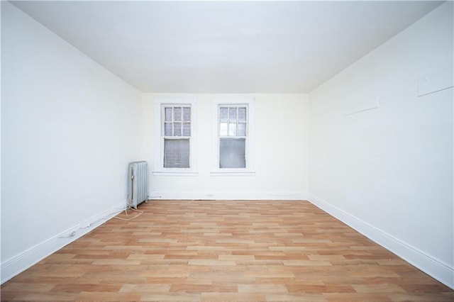 spare room featuring radiator heating unit, light wood-style floors, and baseboards