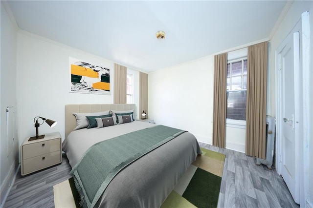 bedroom with wood finished floors, multiple windows, crown molding, radiator heating unit, and baseboards