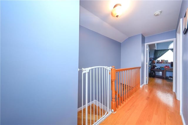 corridor featuring an upstairs landing, lofted ceiling, and light wood-style floors
