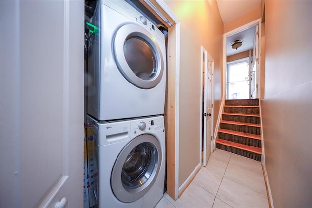 laundry room with light tile patterned floors, stacked washer and clothes dryer, and baseboards