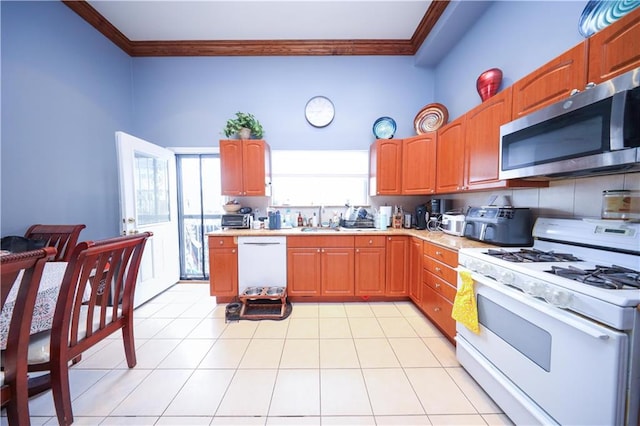 kitchen featuring crown molding, a sink, light countertops, light tile patterned flooring, and white appliances